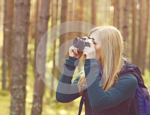 Happy, beautiful blond girl taking pictures in forest. Camp, tourism, hiking concept.