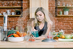 Happy beautiful blond woman standing in her kitchen and writing a shopping list on a notebook at home. Healthy Food -