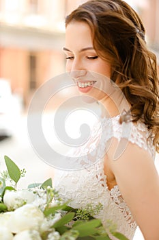 Happy beautiful bride keeping bouquet of flowers and wearing white dress.