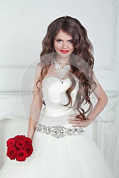 Happy beautiful brunette bride with long wavy hair styling holding red roses bouquet