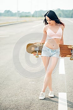 Happy beautiful brunette girl hold her wooden longboard skateboard in back