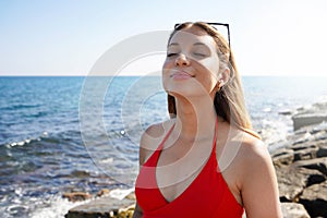 Happy beautiful carefree woman breathing fresh air enjoying wind on the beach. Relaxed bikini woman with closed eyes feeling good