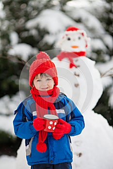 Happy beautiful child building snowman in garden