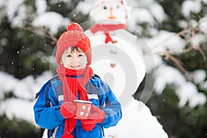 Happy beautiful child building snowman in garden