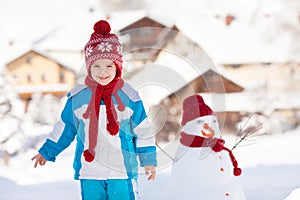 Happy beautiful child building snowman in garden, winter