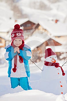 Happy beautiful child building snowman in garden, winter