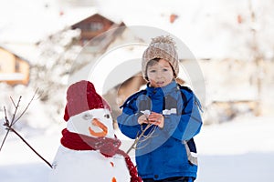 Happy beautiful child building snowman in garden, winter