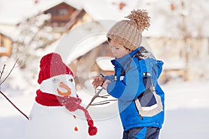 Happy beautiful child building snowman in garden, winter