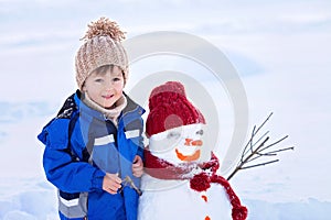 Happy beautiful child building snowman in garden, winter