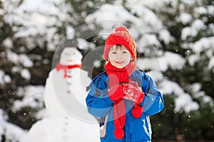 Happy beautiful child building snowman in garden, winter time
