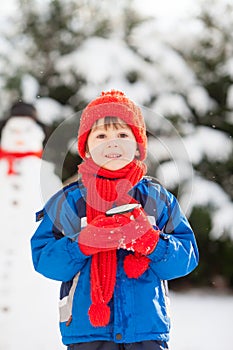 Happy beautiful child building snowman in garden, winter time