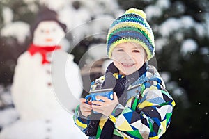 Happy beautiful child building snowman in garden, winter time