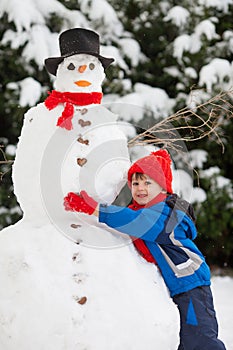 Happy beautiful child building snowman in garden, winter time