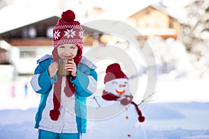 Happy beautiful child building snowman in garden, winter time, h