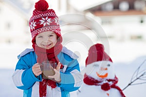 Happy beautiful child building snowman in garden, winter time, h