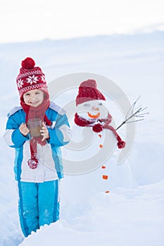 Happy beautiful child building snowman in garden, winter time, h