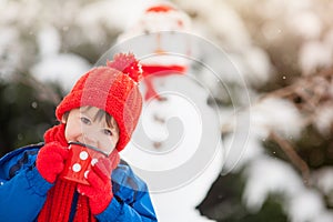 Happy beautiful child building snowman in garden, winter time, h