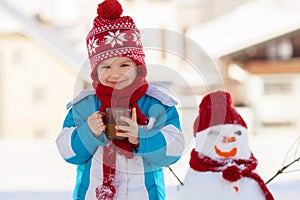 Happy beautiful child building snowman in garden, winter time, h