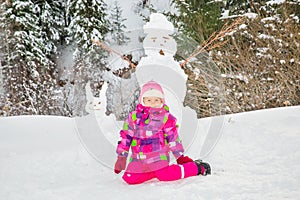 Happy beautiful child girl plaing with a snowman on snowy winter walk.