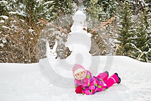 Happy beautiful child girl plaing with a snowman on snowy winter walk.