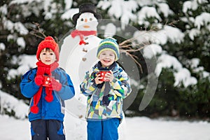 Happy beautiful children, brothers, building snowman in garden