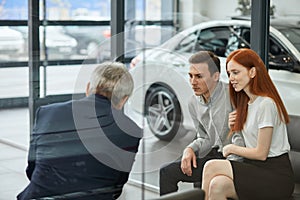Happy beautiful couple is buying a new car at dealership. Family council