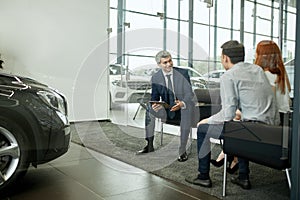 Happy beautiful couple is buying a new car at dealership. Family council