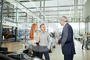 Happy beautiful couple is buying a new car at dealership. Family council