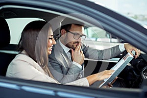 Happy beautiful couple is choosing a new car at dealership