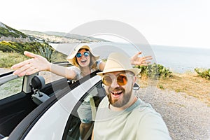 Happy beautiful couple in love taking a selfie portrait driving a convertible car on the road at vacation. Rental cars