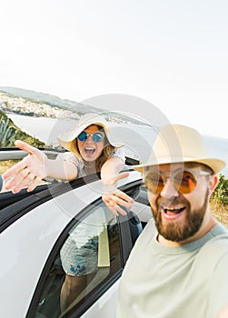 Happy beautiful couple in love taking a selfie portrait driving a convertible car on the road at vacation. Rental cars