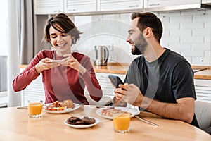 Happy beautiful couple using cellphones while having breakfast