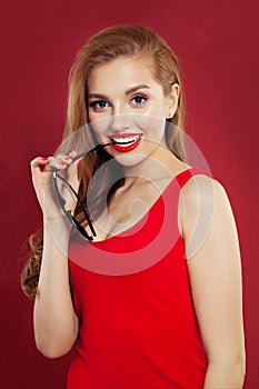 Happy beautiful cute cheerful girl holding sunglasses, smiling and looking at camera over red background. woman portrait