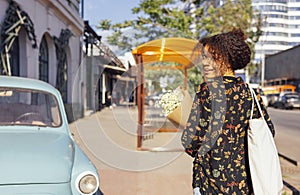 Happy beautiful darkskin girl walks along the street with a bouquet of daisies