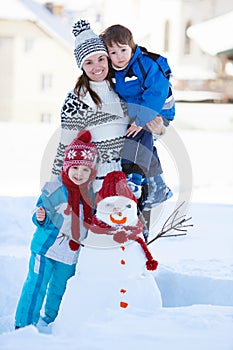 Happy beautiful family building snowman in garden, winter time,