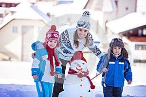 Happy beautiful family building snowman in garden, winter time,