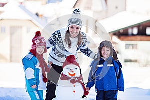 Happy beautiful family building snowman in garden, winter time,