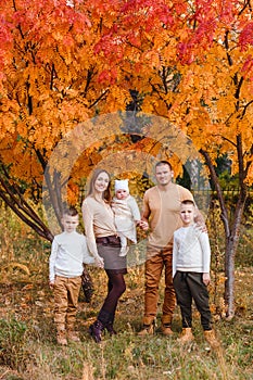 Happy beautiful family of five on walk in the autumn against the background of yellow leaves of mountain ash
