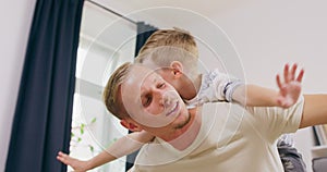 Happy beautiful family healthy young father lifting cute little child boy up playing plane on carpet at home, funny kid