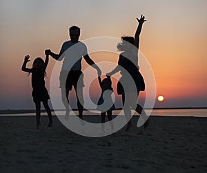 Happy beautiful family jumping on the beach at the sunset