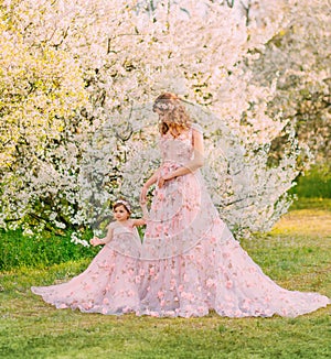 Happy beautiful family mom and daughter, spring blooming garden. Long luxury evening fantasy dresses powder pink color