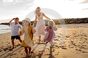 Happy beautiful family relaxing and dancing at the sunset beach in summer. Smiling mother with her two little daughters and one