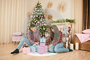 Happy beautiful family sitting on floor with christmas gifts and