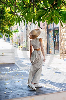 Happy beautiful fashionable woman with a smile wearing a fashionable hat. standing and having fun near a green tree on the street