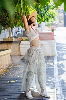 Happy beautiful fashionable woman with a smile wearing a fashionable hat. standing and having fun near a green tree on the street