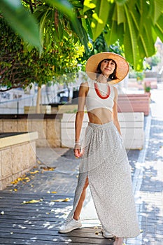 Happy beautiful fashionable woman with a smile wearing a fashionable hat. standing and having fun near a green tree on the street
