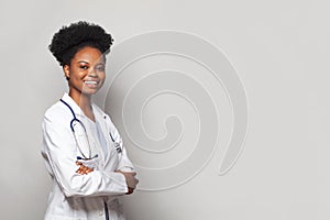 Happy beautiful female doctor in medical coat standing with crossed arms on white banner background