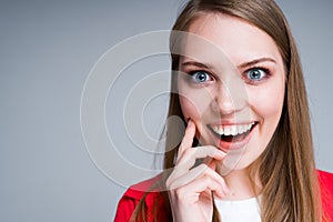 Happy beautiful girl with blue eyes opens her mouth in surprise, touching her chin with her finger