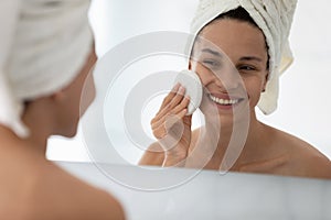 Happy beautiful girl cleansing facial skin with skincare exfoliating sponge