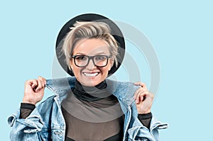 Happy beautiful girl in fashionable jeans jacket and hat on blue background.